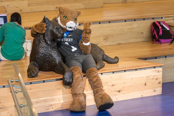 Photo of UK's mascot posing with a wildcat statue in the student center